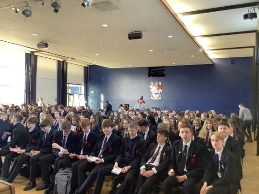 A large group of students wearing school uniform and  sitting in a hall